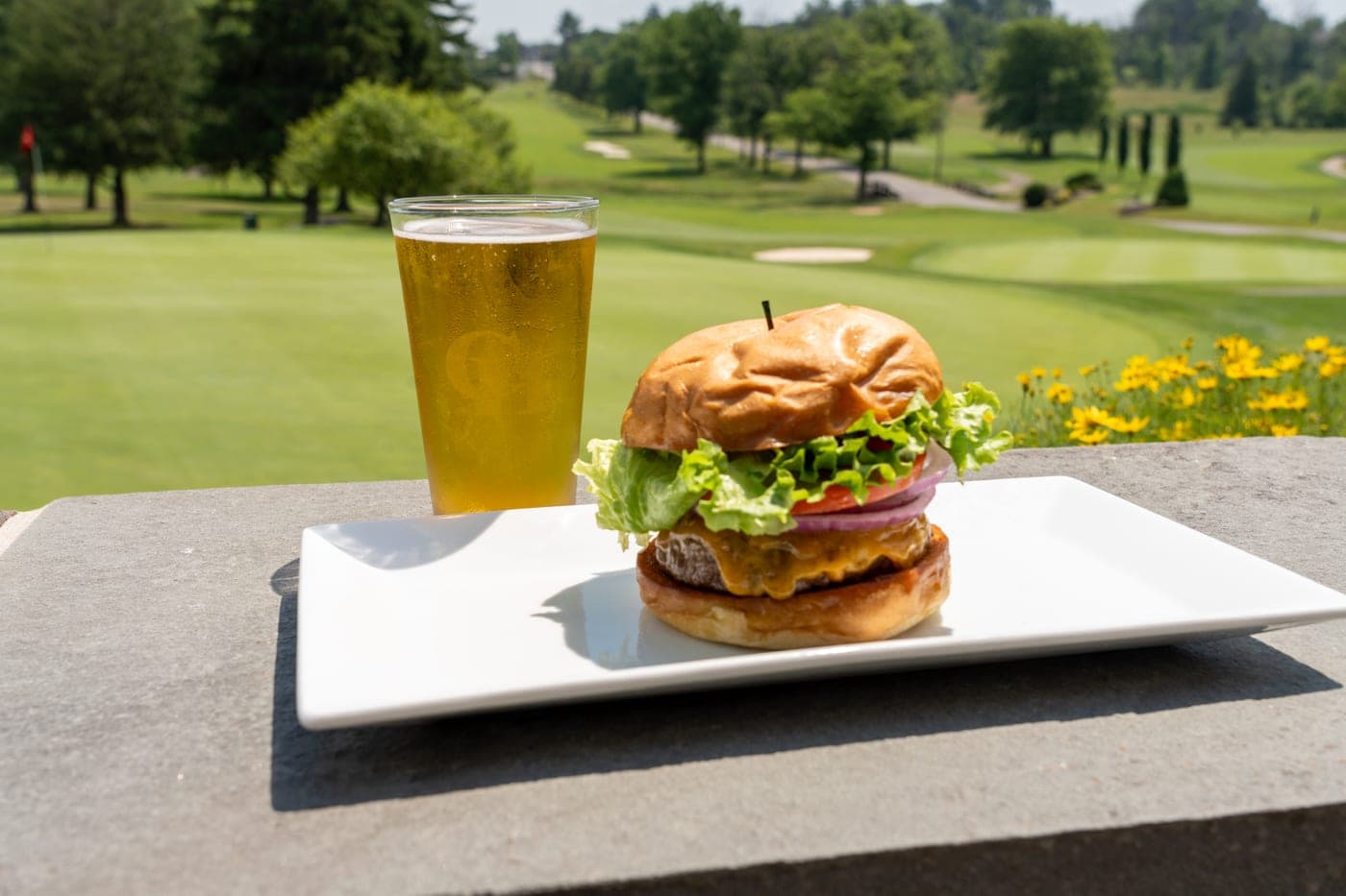 A cheeseburger and a cold beer on the terrace ledge, overlooking a sunlit fairway.