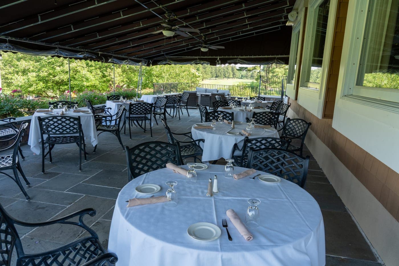 The covered outdoor dining terrace at Copper Hill, tables set with white linen and the course beyond.
