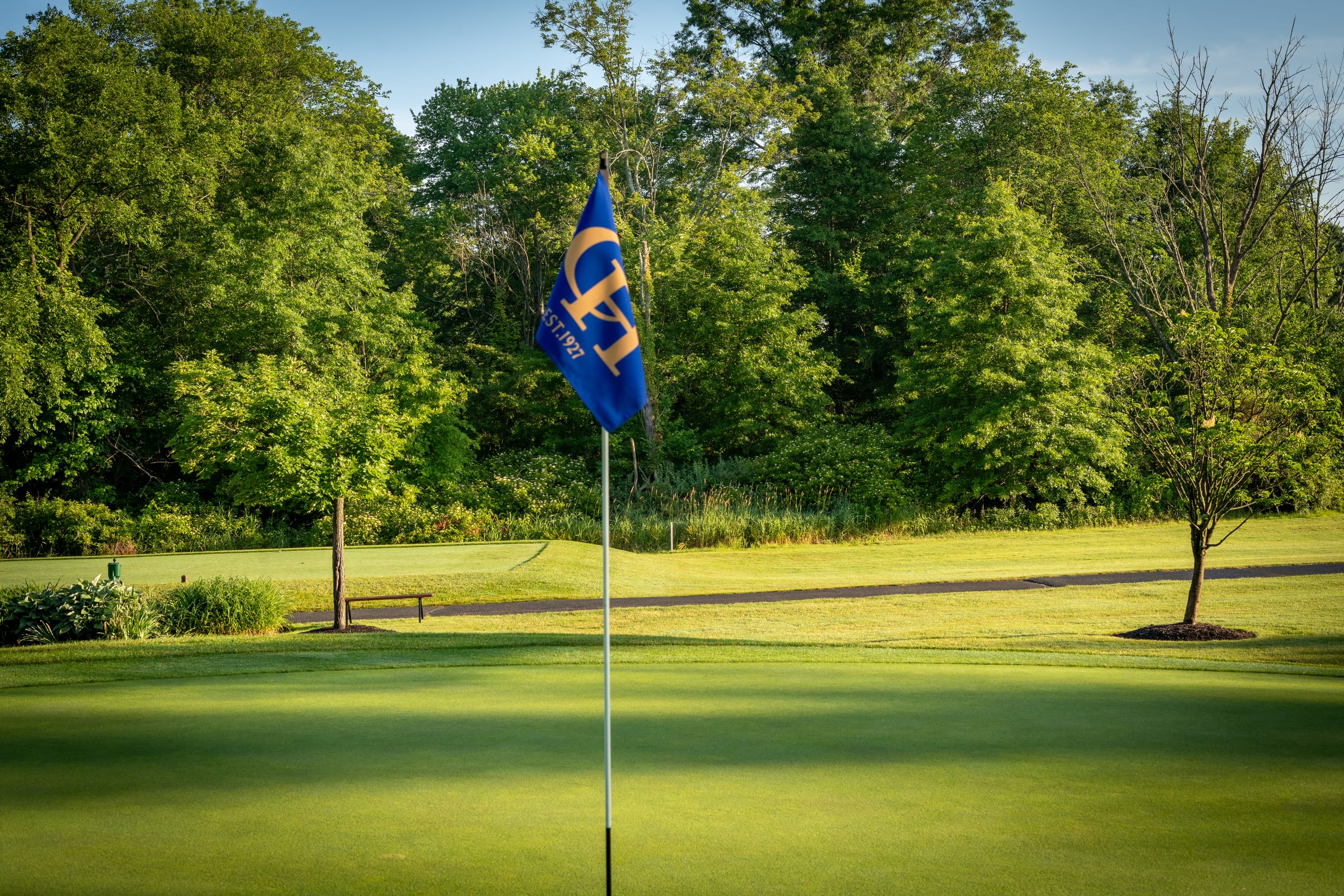 The Copper Hill monogram flag on a putting green at sunrise, the fairway and treeline beyond.